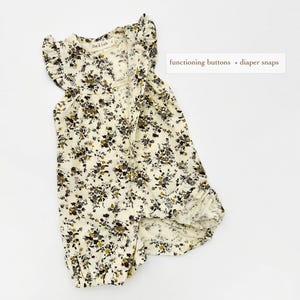 May include: A white floral print baby onesie with ruffled sleeves and a button closure. The onesie has functioning buttons and popper fastenings.