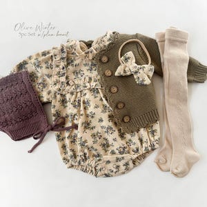 May include: A baby outfit set with a floral print bodysuit, a brown knitted cardigan, a brown knitted hat, and beige tights. The set also includes a brown bow headband.