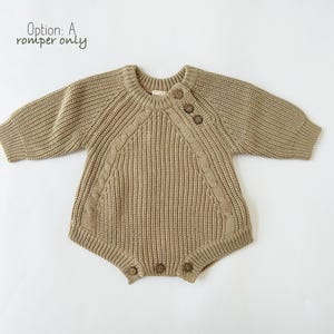 May include: A brown knitted baby romper with a cable knit pattern and wooden buttons. The romper has long sleeves and a round neckline.