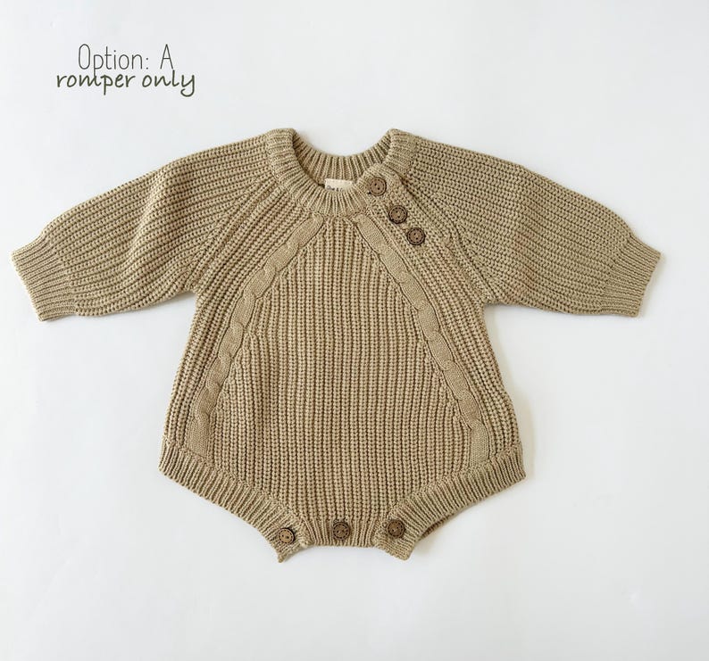 May include: A brown knitted baby romper with a cable knit pattern and wooden buttons. The romper has long sleeves and a round neckline.