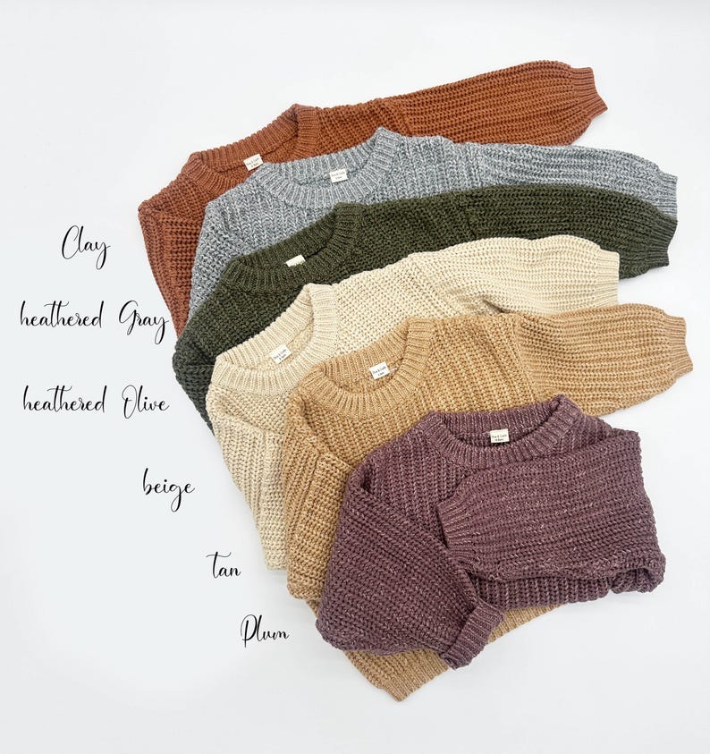 May include: A collection of six long-sleeved knit sweaters in various colors, including clay, heathered gray, heathered olive, beige, tan, and plum. Each sweater features a ribbed crew neckline, ribbed cuffs, and a chunky, textured knit pattern.