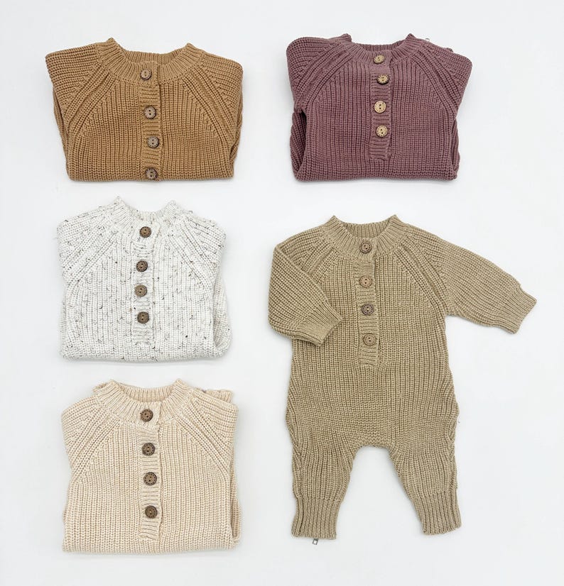 May include: Four knitted baby onesies in different colors and patterns. The onesies have a button closure down the front and long sleeves. The colors are brown, beige, white with brown speckles, and purple.