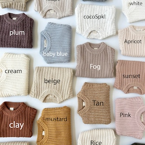 May include: A collection of folded knit sweaters in various colors labeled with text including Oregano, Taupe, gray, milk white, plum, cocoSpkl, baby blue, Apricot, cream, beige, Fog, sunset, clay, mustard, Tan, Pink, Rice, and olive.