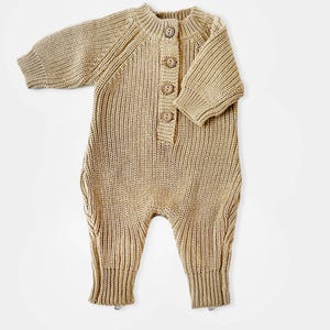 May include: A tan knitted baby onesie with long sleeves and a button closure at the neck.