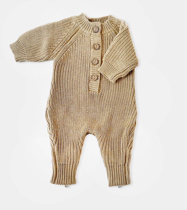 May include: A tan knitted baby onesie with long sleeves and a button closure at the neck.