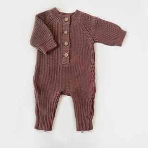 May include: A mauve knitted baby onesie with long sleeves and a button closure at the front.