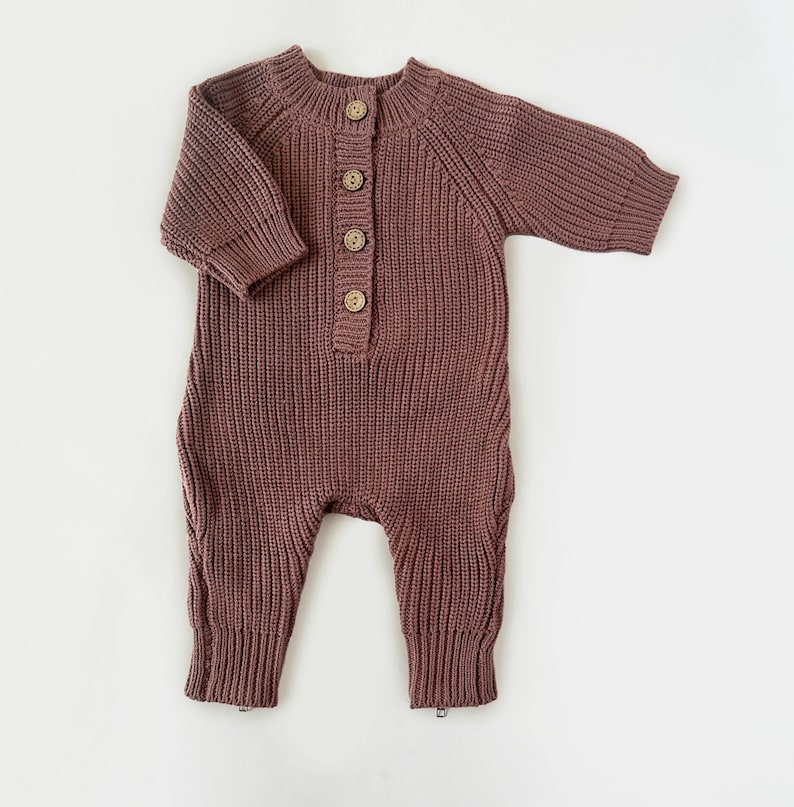 May include: A mauve knitted baby onesie with long sleeves and a button closure at the front.