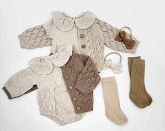 May include: Two baby outfits with a gingham and knit pattern. One outfit is brown and the other is beige. Both outfits have a ruffled collar and button closure. The outfits are paired with matching knit socks and headbands.