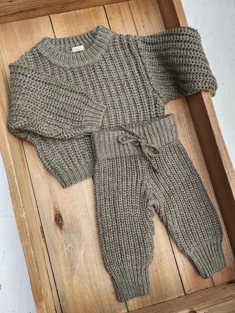 May include: A green knitted sweater and matching pants set for a baby or toddler. The sweater has a round neckline and long sleeves. The pants have a drawstring waistband and a relaxed fit.