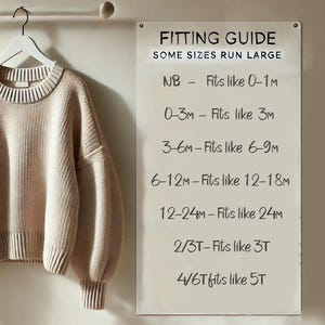 May include: A beige long-sleeve knit sweater hangs on a white hanger next to a white sign titled FITTING GUIDE. The text reads: SOME SIZES RUN LARGE, NB - Fits like 0-1M, 0-3M - Fits like 3M, 3-6M - Fits like 6-9M, 6-12M - Fits like 12-18M, 12-24M - Fits like 24M, 2/3T - Fits like 3T, 4/6T fits like 5T.