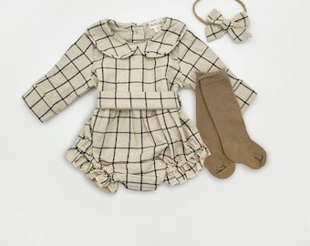 May include: A beige and black plaid baby outfit set, including a long-sleeved romper with a Peter Pan collar, a matching headband with a bow, and a pair of knee-high socks. The outfit is made of a soft fabric.