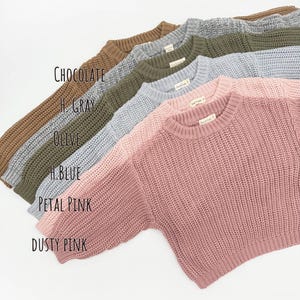 May include: A collection of six long-sleeve knit sweaters with a ribbed crew neckline and cuffs, displayed in a stacked diagonal arrangement. The colors are labeled as Chocolate, H. Gray, Olive, H. Blue, Petal Pink, and Dusty Pink.