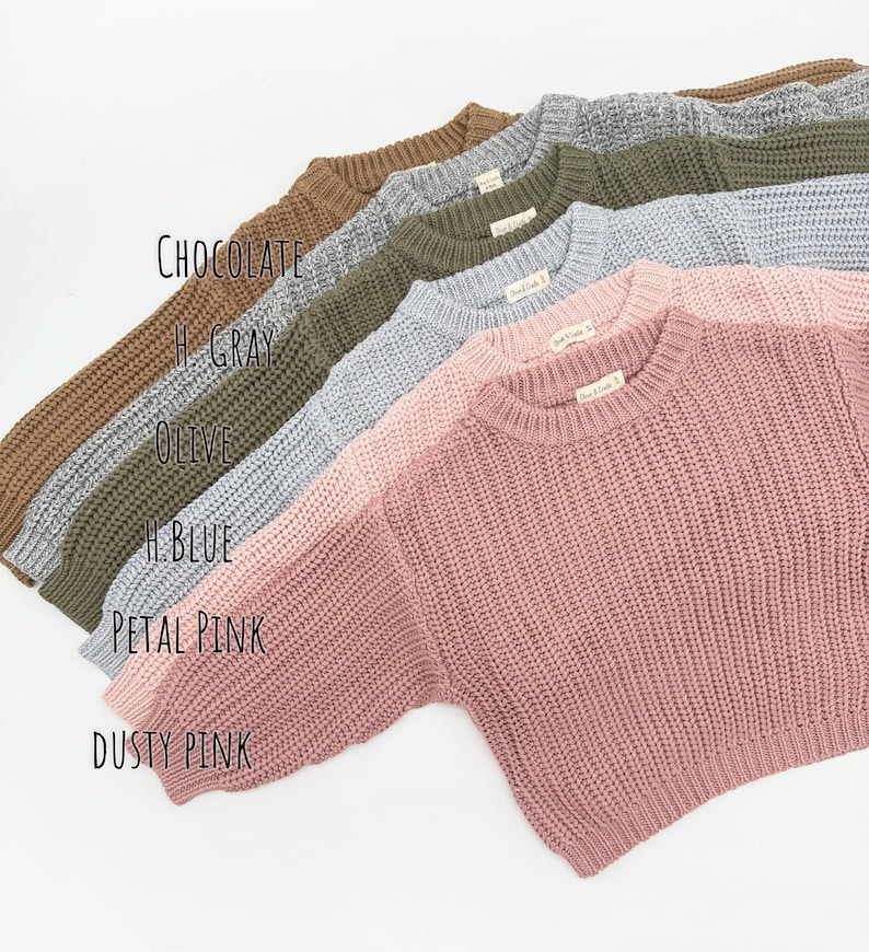 May include: A collection of six long-sleeve knit sweaters with a ribbed crew neckline and cuffs, displayed in a stacked diagonal arrangement. The colors are labeled as Chocolate, H. Gray, Olive, H. Blue, Petal Pink, and Dusty Pink.