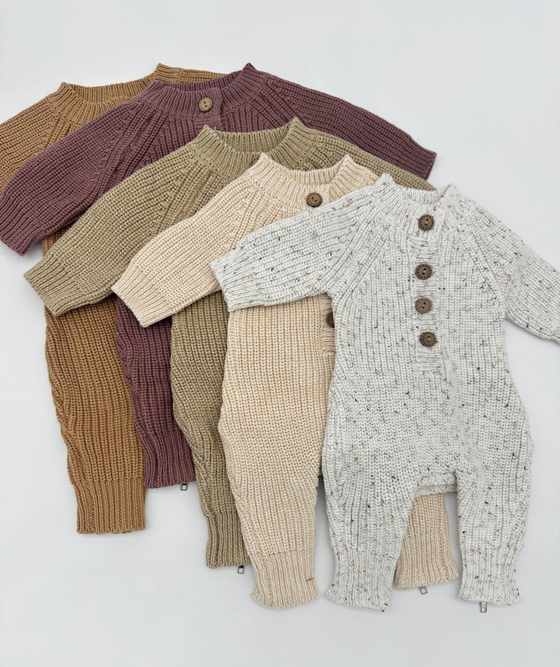 May include: Five knitted baby onesies in different colors, including beige, brown, cream, and white with speckles. The onesies have a button closure and long sleeves.