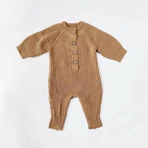 May include: A brown knitted baby onesie with a button closure at the neckline. The onesie has long sleeves and a ribbed texture.