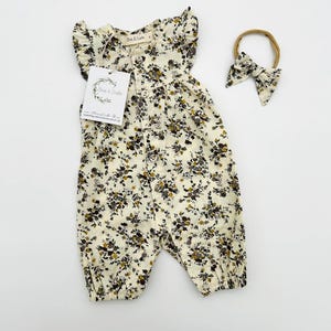 May include: A white floral print baby onesie with ruffled sleeves and a button closure. The onesie is paired with a matching brown headband.