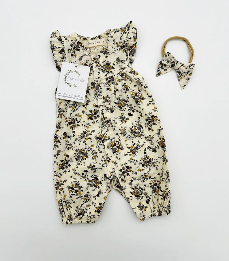 May include: A white floral print baby onesie with ruffled sleeves and a button closure. The onesie is paired with a matching brown headband.