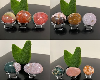 May include: A collection of six polished, colourful, and patterned stones on display stands. The stones are various shades of red, pink, brown, green, and purple.