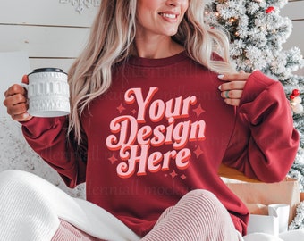 May include: A woman wearing a red sweatshirt with the text "Your Design Here" in pink and white lettering. She is sitting on a white blanket with a Christmas tree in the background.