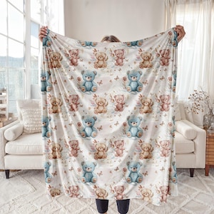 May include: A white blanket with a repeating pattern of watercolour teddy bears in blue, pink, and tan. The design includes butterflies and floral accents, creating a whimsical and comforting aesthetic.