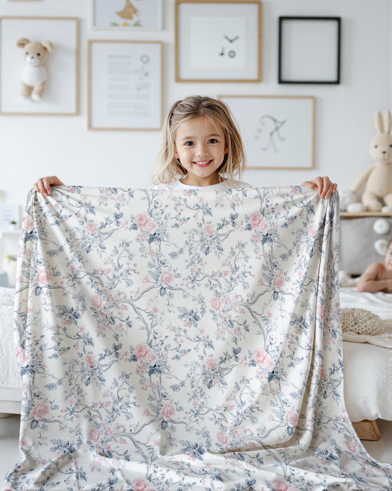 Pode incluir: Um tecido branco com estampa floral em rosa e azul. Uma menina est&aacute; segurando o tecido na frente dela.