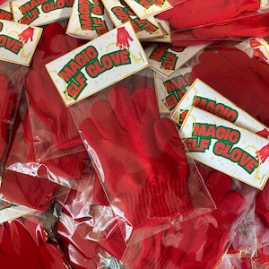 May include: A pile of red knit gloves, each packaged in a clear plastic bag with a decorative tag. The tag reads "MAGIC ELF GLOVE" in green and red lettering, with a small illustration of a hand.