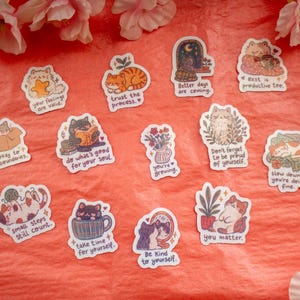 May include: A collection of thirteen individual die-cut stickers featuring various illustrated cats in different poses and settings, each accompanied by motivational text such as 'your feelings are valid', 'trust the process', and 'you matter'.