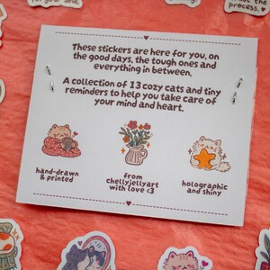May include: A white rectangular card featuring text about a collection of 13 cat stickers. The card displays illustrations of a cat with a mug, a flower vase, and a cat holding a star. Surrounding the card are various cat-themed stickers.