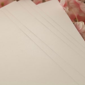 May include: A stack of white card stock paper with a smooth, textured surface.