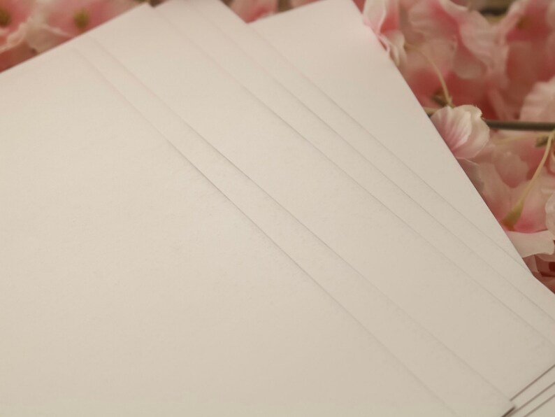 May include: A stack of white card stock paper with a smooth, textured surface.