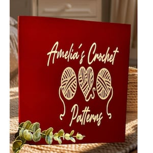 May include: A red wooden sign with gold lettering that reads "Amelia's Crochet Patterns". The sign features two balls of yarn and a heart.