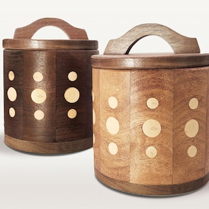 May include: Two wooden canisters with lids and handles. One is dark brown, the other is light brown. Both have a series of inlaid, circular, light-colored accents. The canisters are cylindrical with a curved handle on top.