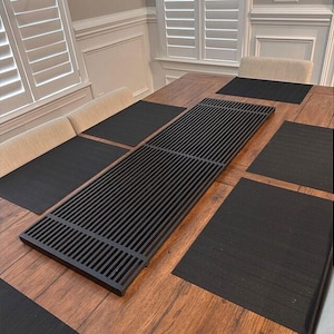 May include: A black metal table runner with a slatted design sits on a wooden table with black placemats.