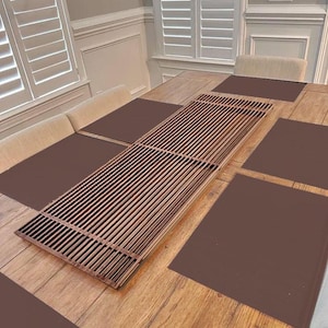 May include: A wooden table setting featuring a long, rectangular, slatted wooden centerpiece. The table is set with brown placemats. The room has white shutters and a light-colored bench.