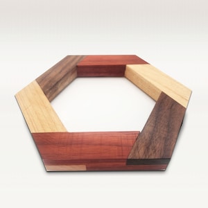 May include: A hexagonal wooden coaster made of different types of wood, including walnut, maple, and cherry. The coaster has a natural wood finish and is designed to protect surfaces from heat and scratches.