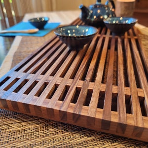 May include: A wooden tea tray with a slatted design. The tray is made of dark brown wood and has a natural finish. The tray is perfect for serving tea and other beverages.