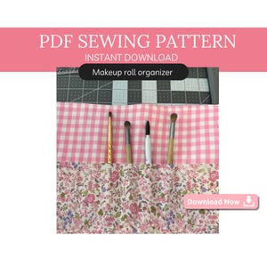 以下が含まれることがあります： メイクロールオーガナイザーのPDF縫製パターン。パターンはピンクと白のギンガムチェック生地と花柄生地を使用しています。画像は、メイクブラシが入った完成品を示しています。