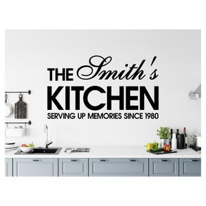 Puede incluir: Adhesivo de pared negro con el texto "THE Smith's KITCHEN SERVING UP MEMORIES SINCE 1980". El adhesivo está encima de una encimera de cocina con un fregadero, armarios y varios artículos de cocina.