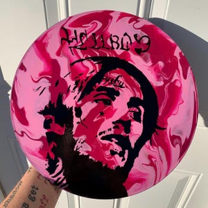 May include: A circular disc featuring a marbled pink and magenta background with a black silhouette portrait of a person. The text HELLBOY is printed in black at the top, and the word Peep is written in black script above the person's forehead.