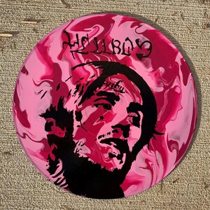 May include: A circular vinyl record featuring a pink and white marbled background with a black silhouette portrait of a person. The text HELLBOY is printed in a stylized black font at the top, and the word baby is visible on the forehead area.