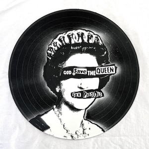 May include: Black and white vinyl record featuring a stencil image of Queen Elizabeth II with the text "GOD Save the QUEEN" and "SEX PISTOLS" in a bold, blocky font. The record has a radial groove pattern.