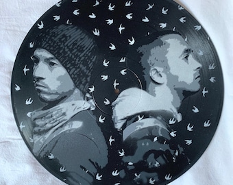 May include: A black vinyl record with a white silhouette of two people facing away from each other. The background is filled with small white birds.