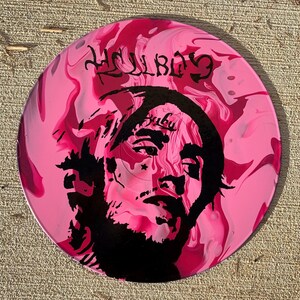 May include: A circular disc featuring a marbled pink and magenta background with a black silhouette portrait of a person with facial tattoos. The text HELLBOY is printed in a stylized black font at the top, and the word BABY is visible on the forehead.
