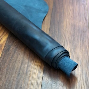 May include: A roll of dark blue leather, rolled up and lying on a wooden surface.