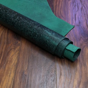 May include: A roll of dark green embossed leather with a floral pattern. The leather is rolled up and lying on a wooden surface.