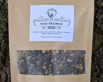 May include: A brown paper bag with a white label that reads "Anxie-TEA Blend" and lists the ingredients: Jasmine, Lemon Balm, Mimosa Blooms, Chamomile, Hibiscus, Skull Cap & Lavender. The label also includes instructions to steep the tea in hot water for 5 minutes. The bag contains a blend of dried herbs.