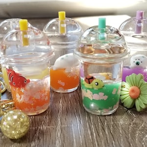 May include: A collection of clear, bubble tea-style keychains with various colorful fillings and miniature animal figures. Each keychain has a gold-colored clasp and a straw. The fillings include pink, orange, and green liquids.