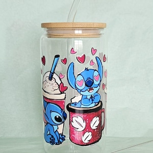 Puede incluir: Un vaso de vidrio transparente con tapa de bamb&uacute; y pajita de vidrio, con un gr&aacute;fico del personaje azul Stitch sentado en una taza roja y junto a una bebida, rodeado de corazones rosas. El texto Choice B es visible en la esquina superior.