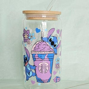 Puede incluir: Un vaso de cristal transparente con tapa de bamb&uacute; y pajita de cristal, con un gr&aacute;fico de un personaje alien&iacute;gena azul y un vaso de bebida helada morado con un logo de sirena. El texto "Choice A" aparece arriba y se incluye un cepillo limpiador.