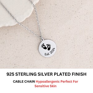 May include: A silver necklace with a round pendant featuring a pair of baby footprints with hearts in the center. The pendant is engraved with "Est. 2024". The necklace is made of 925 sterling silver with a cable chain and is hypoallergenic.